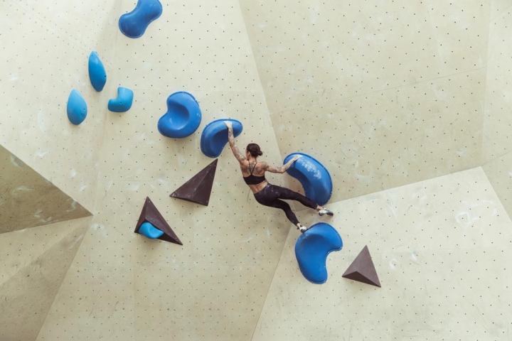Female climber on well set bouldering bloc with large blue holds and volumes